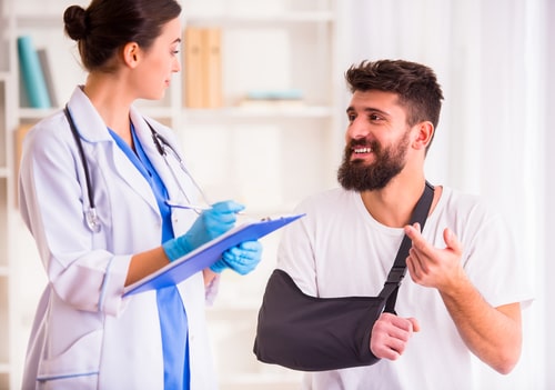 A man in an arm sling with a broken arm speaks to his doctor