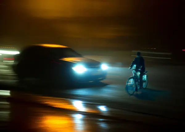 A car speeds toward a cyclist in the middle of the road.