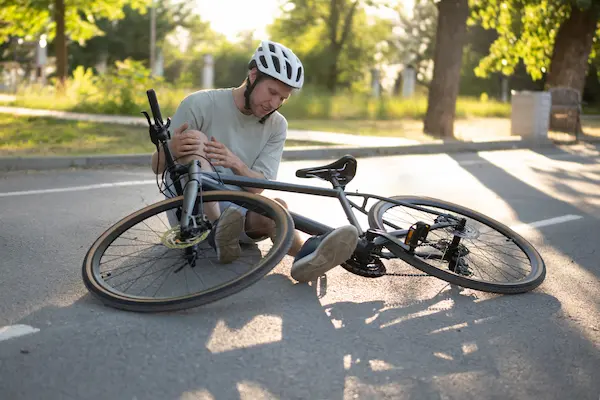 A bicycle accident injury. The rider cradles an injured knee on the ground.