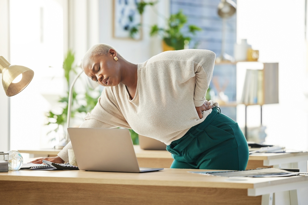 A picture of a woman leaning on her desk at work - dealing with a back strain injury.
